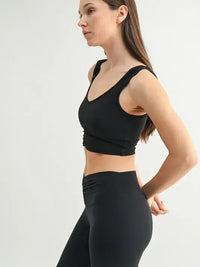 Side view of a woman wearing a MONO B ruched active tank top paired with black leggings.