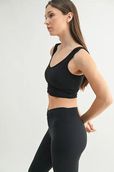 Side view of a woman wearing a MONO B ruched active tank top paired with black leggings.