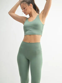 Model in a green activewear U-back tank top and matching leggings, showcasing stylish fitness apparel.