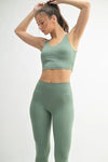Model in a green activewear U-back tank top and matching leggings, showcasing stylish fitness apparel.