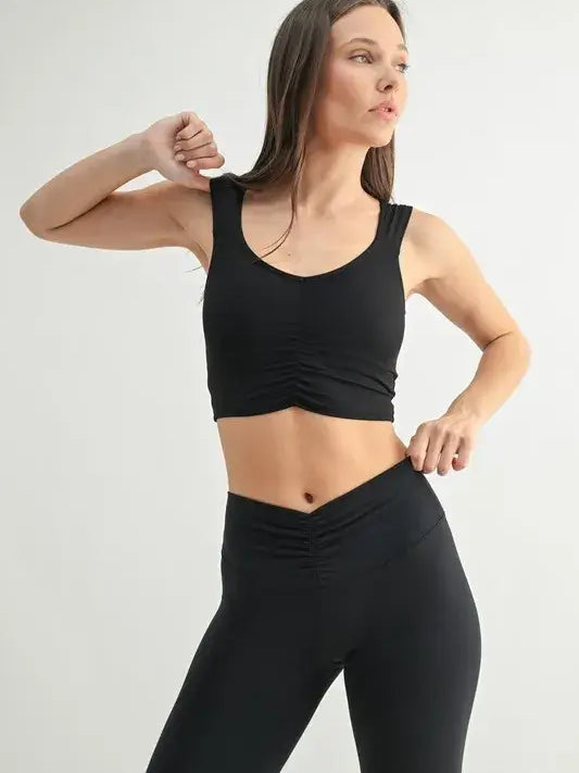 Woman wearing a stylish MONO B ruched active tank top paired with black leggings, showcasing a flattering silhouette.